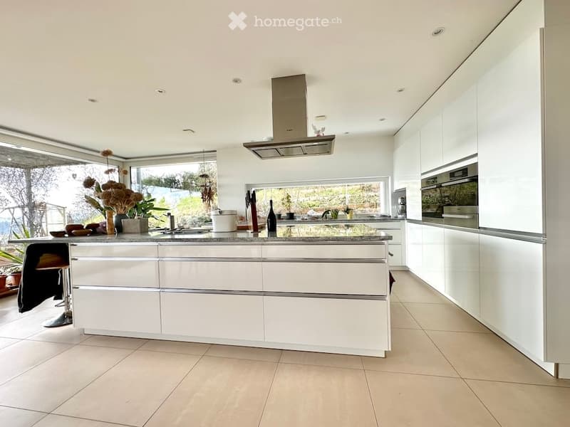 Modern kitchen with white cabinets, a central island, stainless steel appliances, and large windows offering a view of the outdoors.