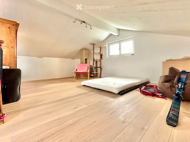Loft-style bedroom with wooden flooring, slanted ceiling, large windows, bed, chair, cat tree, and skateboard.