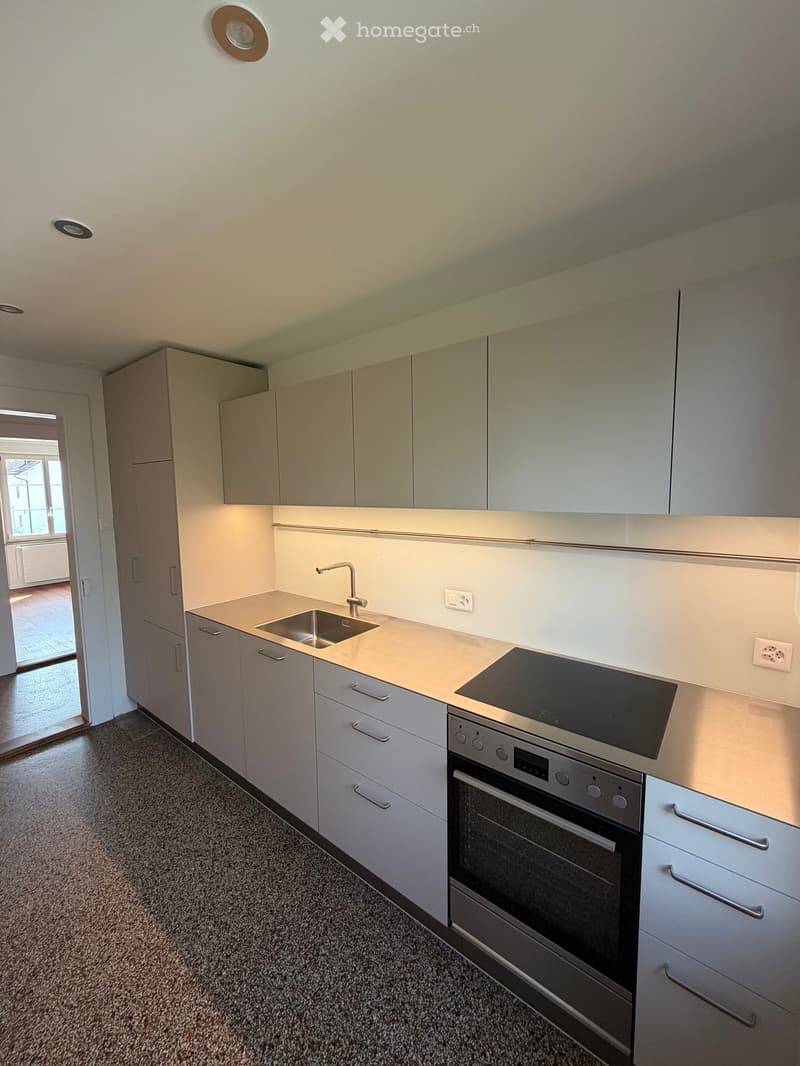 Modern kitchen with light-colored cabinets, a sink, an oven, and an induction cooktop. The space is well-lit with recessed ceiling lights and has a clean, minimalist design.