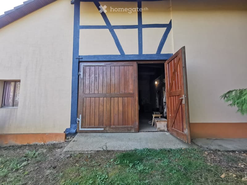 Two-story building with a wooden garage door and a small wooden bench visible inside the open garage.