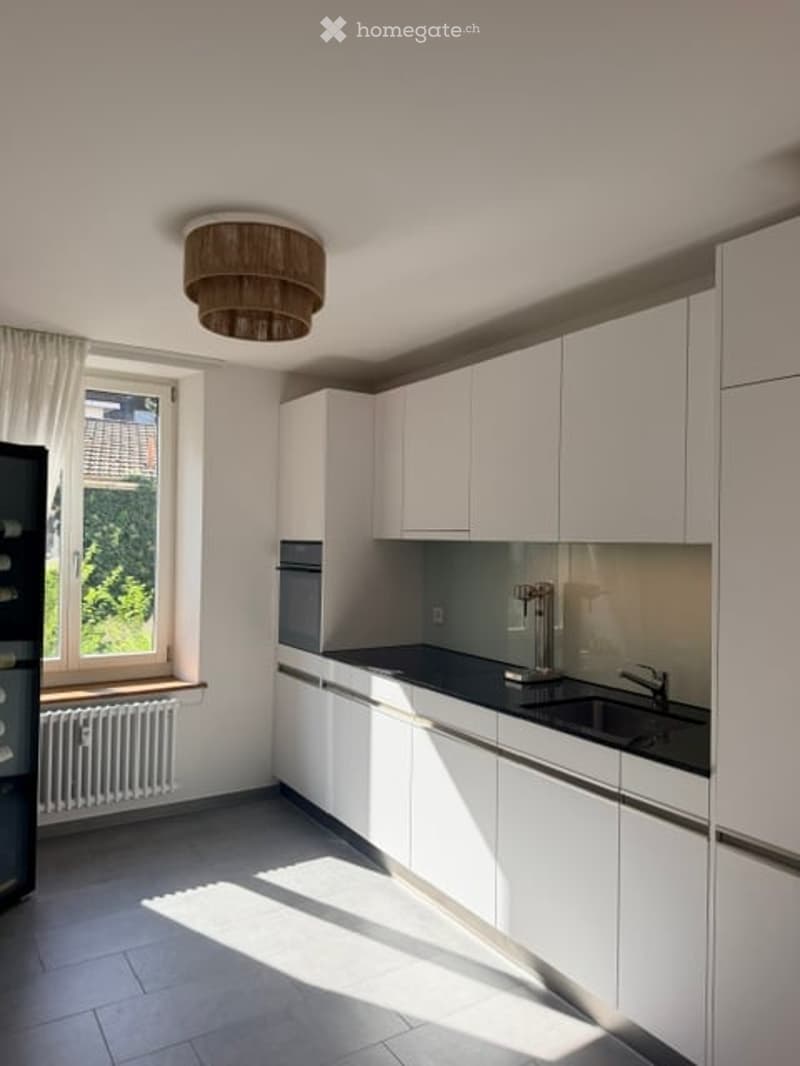 Modern kitchen with white cabinets, black countertop, stainless steel sink, and a window with a view of greenery.
