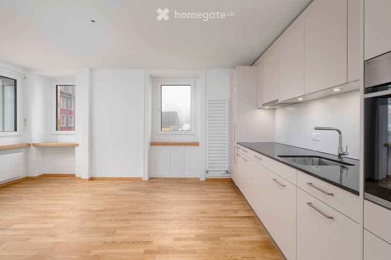 Modern kitchen with white cabinets, wooden flooring, and stainless steel sink.