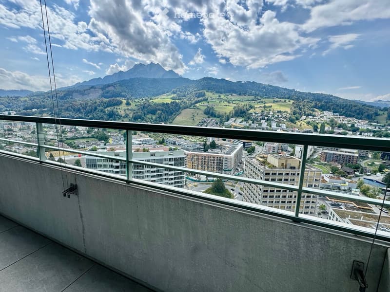 Balcony with a panoramic view of a cityscape and surrounding mountains under a partly cloudy sky.