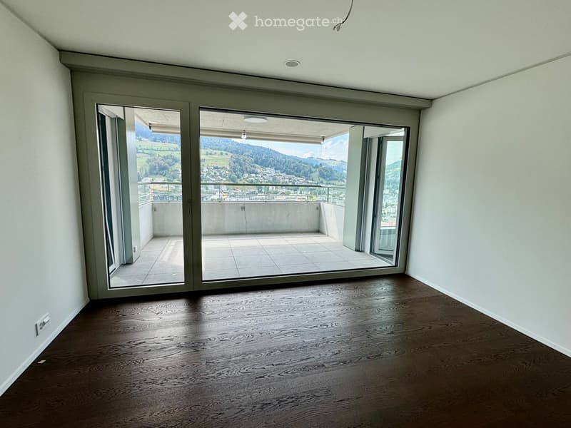 Empty room with wooden flooring, large sliding glass doors leading to a balcony with scenic mountain views.