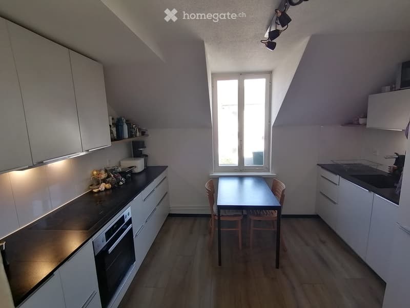 Modern kitchen with white cabinets, black countertops, and a dining area featuring a table and chairs. The space includes an oven, sink, and various appliances.