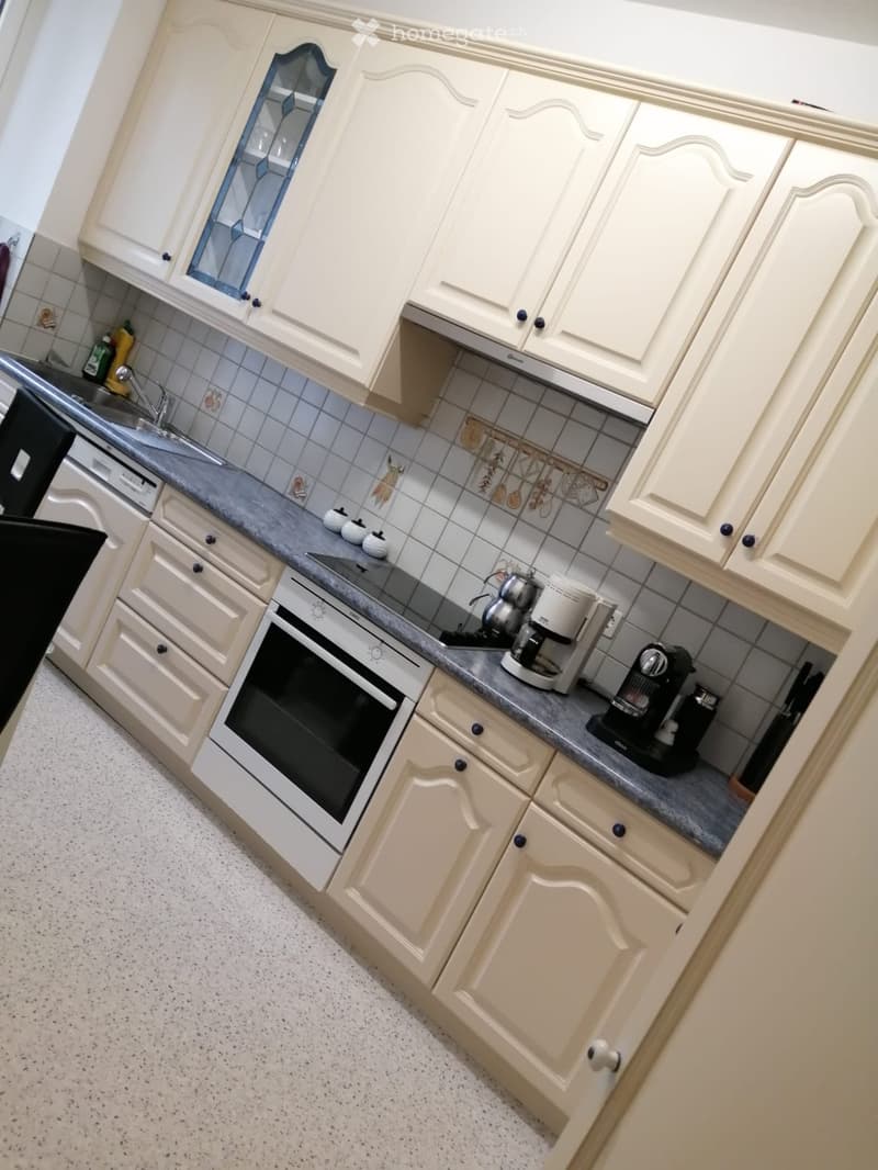 A modern kitchen with white cabinets, a built-in oven, coffee maker, sink, and tiled backsplash.