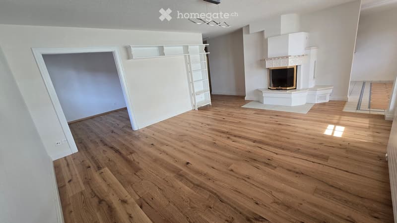 Empty living room with wooden flooring, white walls, fireplace, and built-in shelving unit.