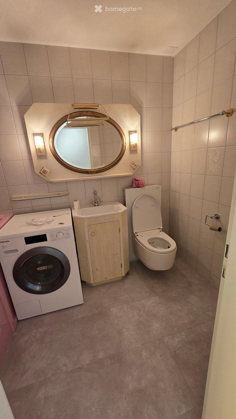 Bathroom with a washing machine, sink, toilet, round mirror, and light fixtures.