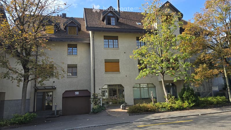 Multi-story residential building with beige facade, multiple windows, and a garage entrance.