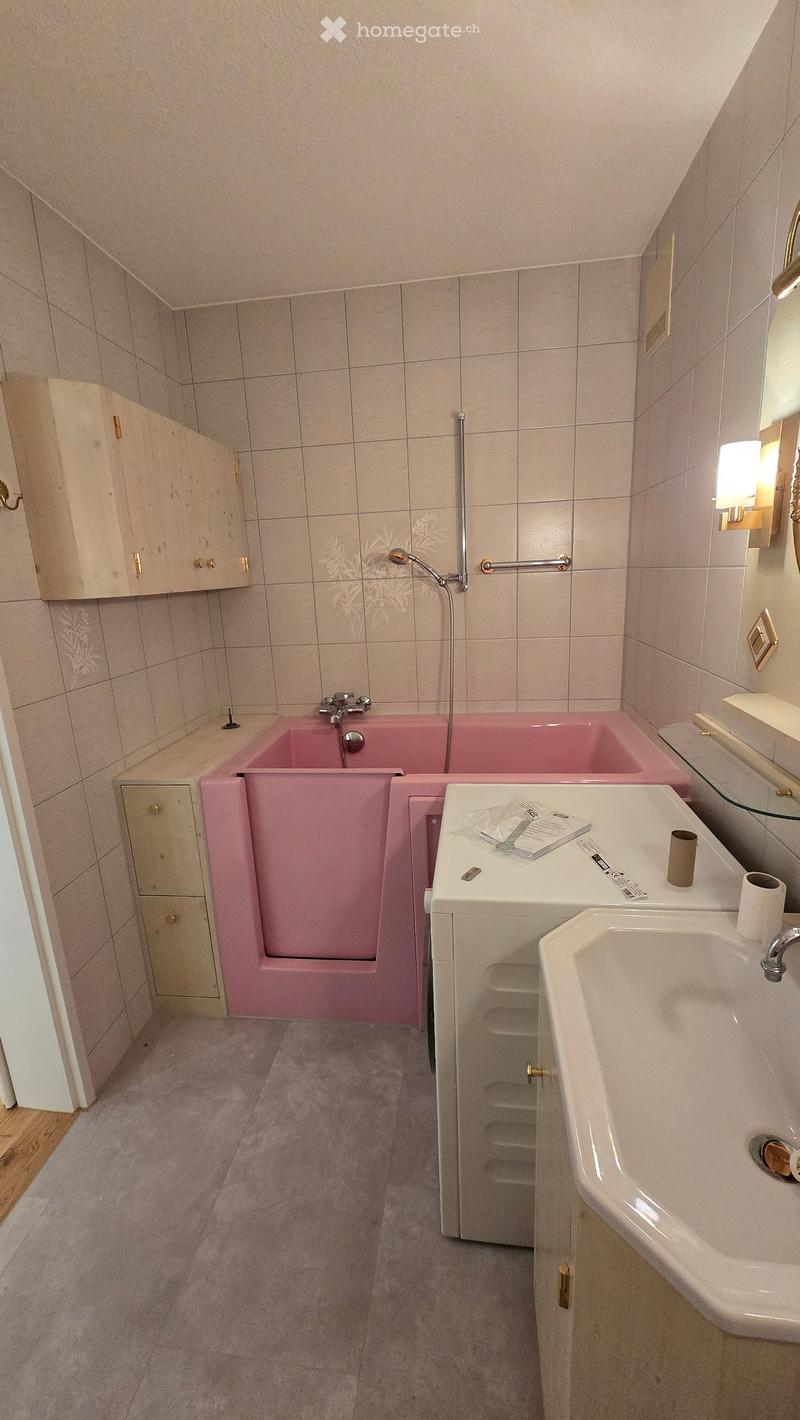 Bathroom with a pink bathtub, white sink, mirror, and wooden cabinets.