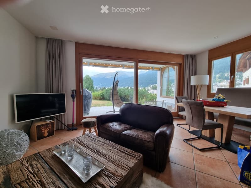 Modern living room with large windows offering a scenic mountain view, featuring a leather sofa, wooden coffee table, dining table, chairs, and a floor lamp.