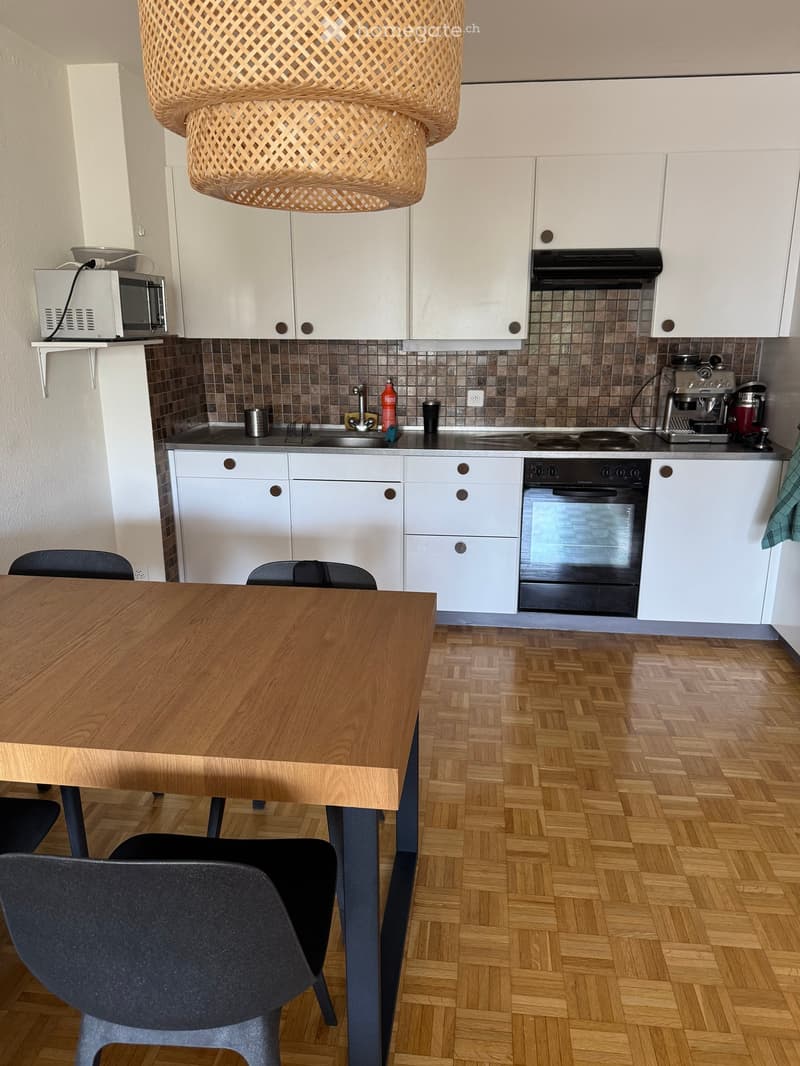 Modern kitchen with white cabinets, wooden table, chairs, and various appliances including a microwave, coffee maker, and oven.
