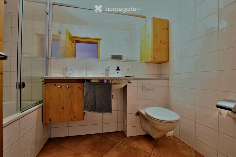 Modern bathroom with a toilet, sink, mirror, wooden cabinet, and a glass-enclosed shower area.