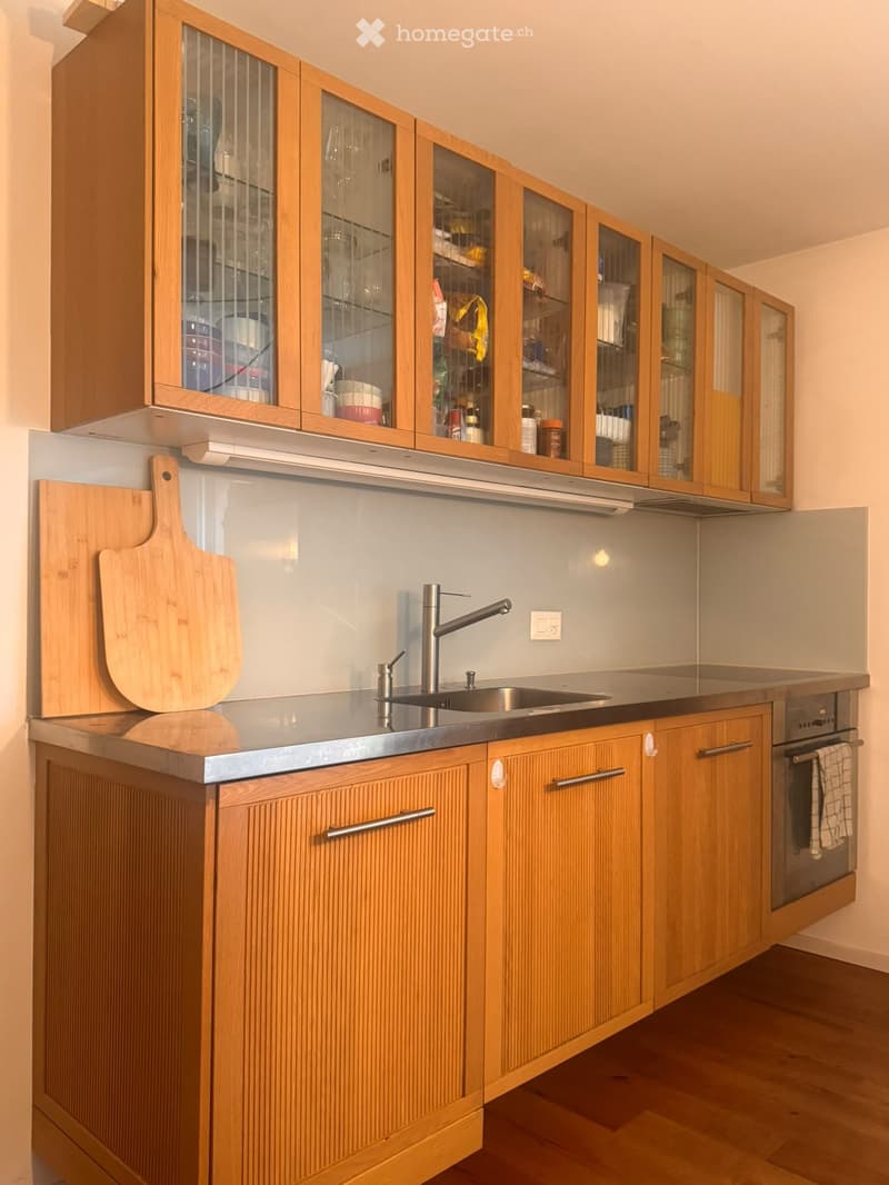 Modern kitchen with wooden cabinets, stainless steel sink, and a cutting board on the counter.
