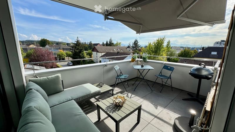 Balcony with a view of the city, featuring a sofa, small tables, chairs, a grill, and potted plants.