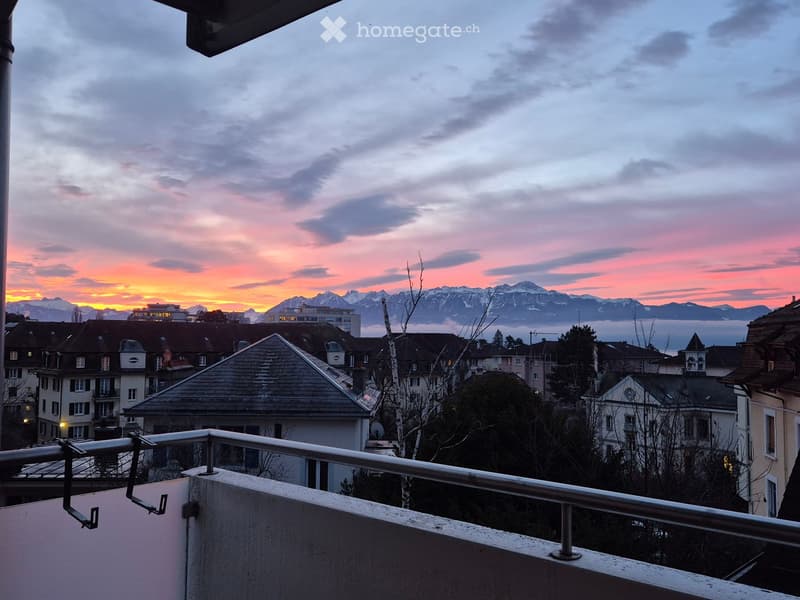 Balcony overlooking a cityscape with rooftops and distant mountains during sunset.