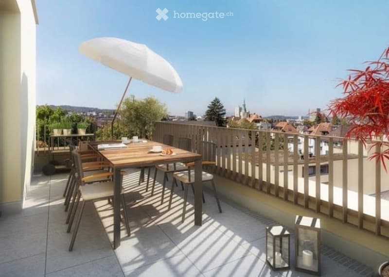 Balcony with a wooden dining table, chairs, and a large umbrella, overlooking a cityscape with trees and buildings.