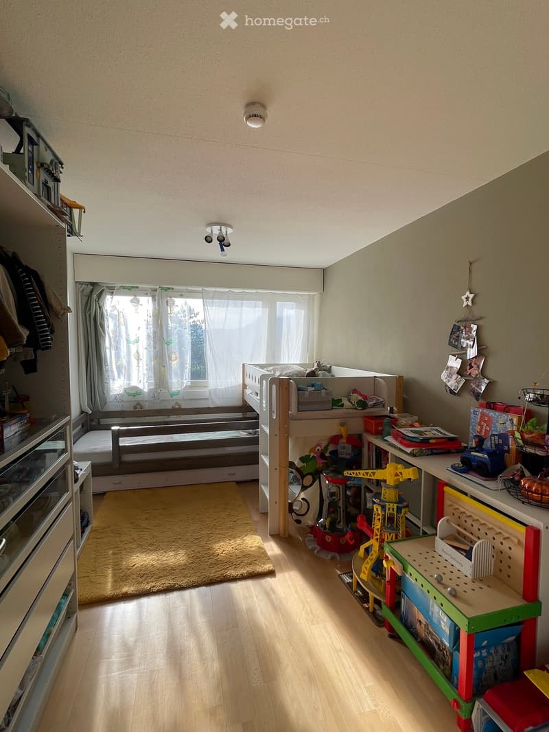 A cozy children's bedroom with a lofted twin-sized bed, colorful toys, shelves, and a window with curtains.