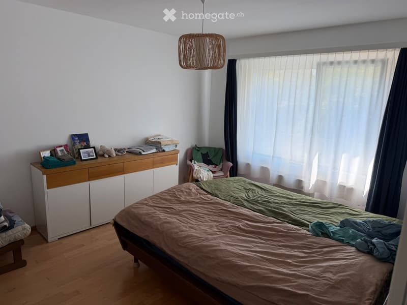Bedroom with a double bed, a wooden cabinet, a pink armchair, and a hanging woven lamp.