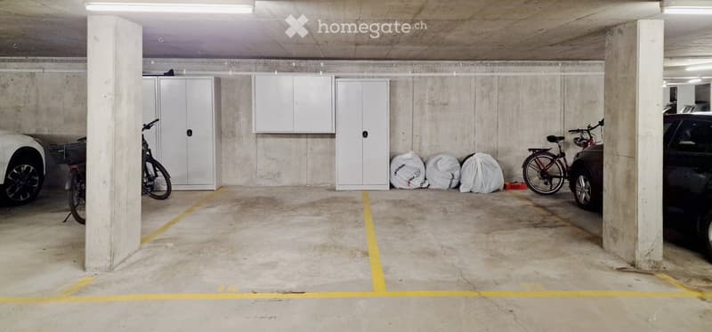 Underground parking area with marked parking spaces, cabinets, bicycles, and storage bags.