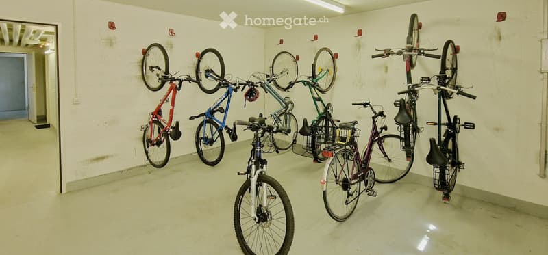 Empty room with white brick walls and concrete floor, several bicycles mounted on wall racks.