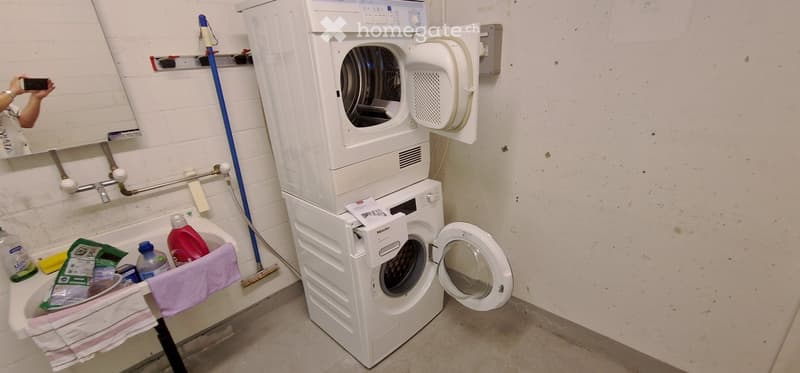 Bathroom with a stacked washer and dryer unit, a mirror, cleaning supplies, and a towel on a small table.