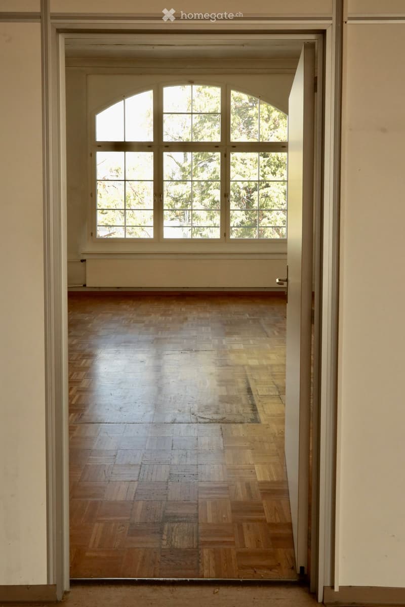 Empty room with wooden flooring and large windows, no furniture or equipment present.