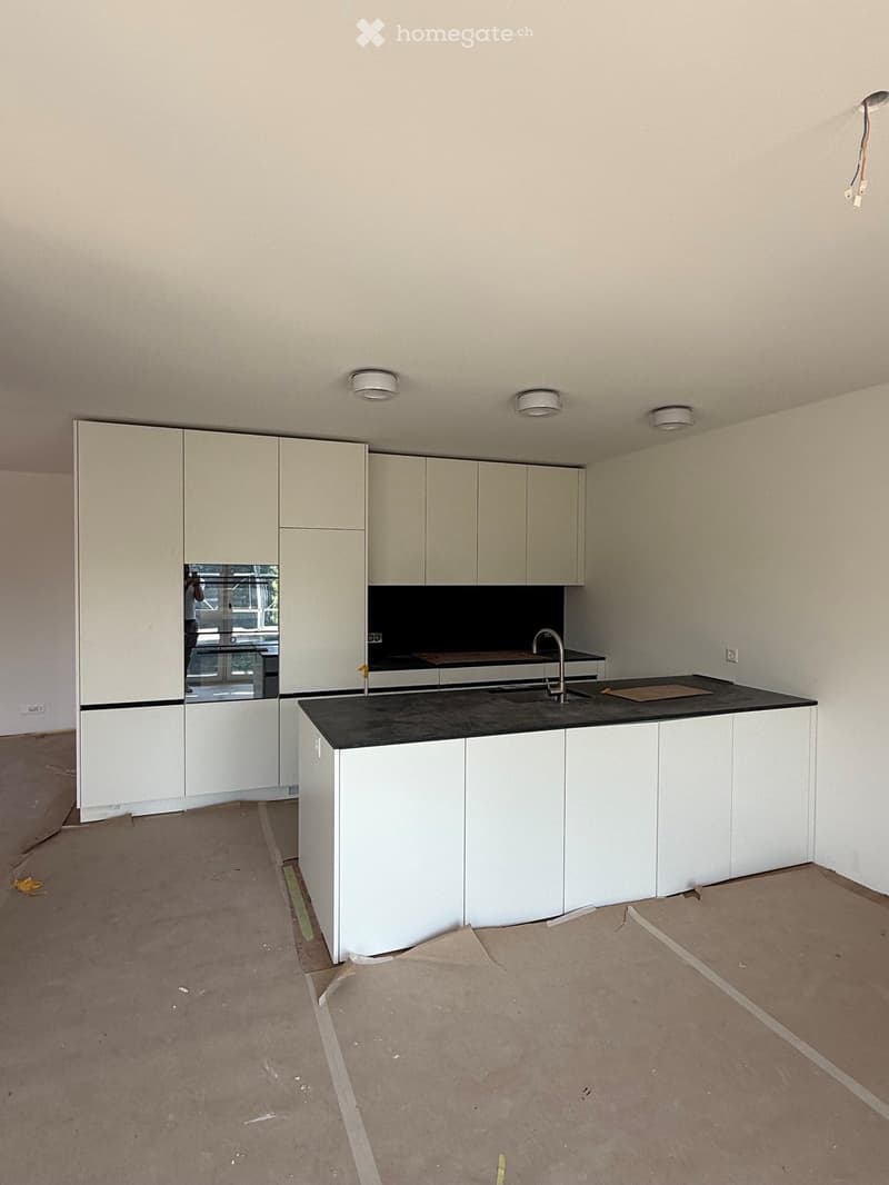 Empty kitchen with white cabinets, black countertop, and stainless steel sink. No appliances or furniture present.
