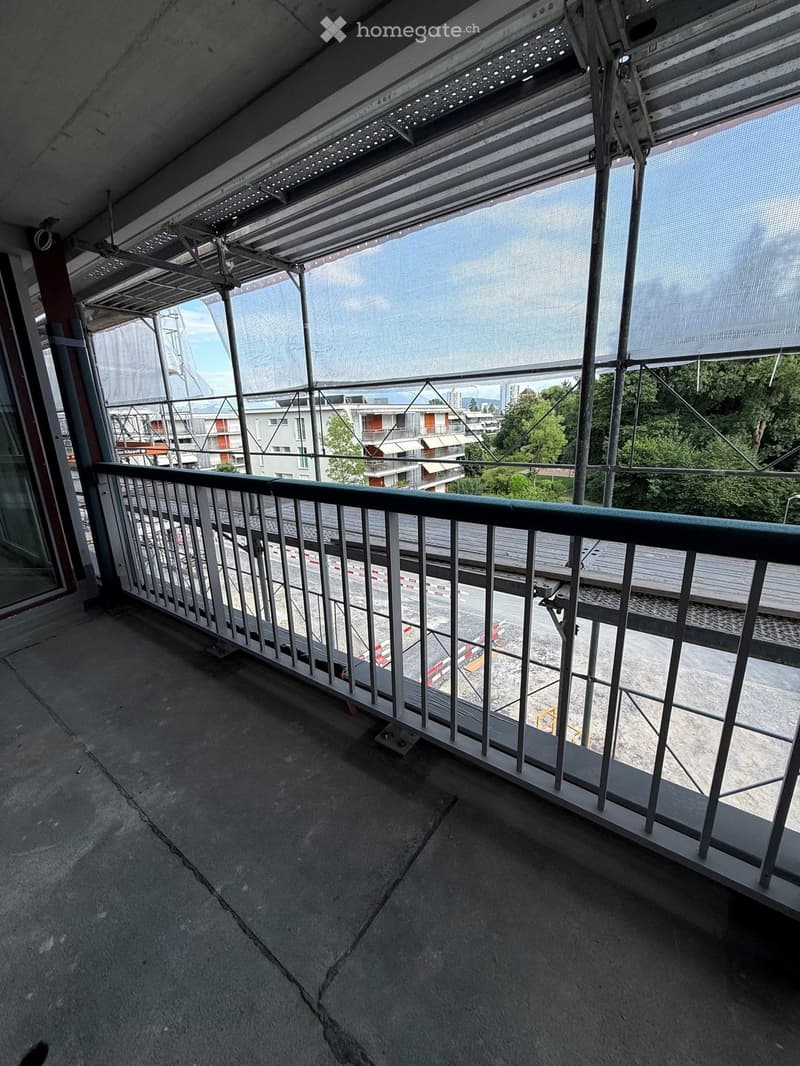 Empty balcony with metal railing, concrete floor, and a view of a construction site and surrounding buildings.