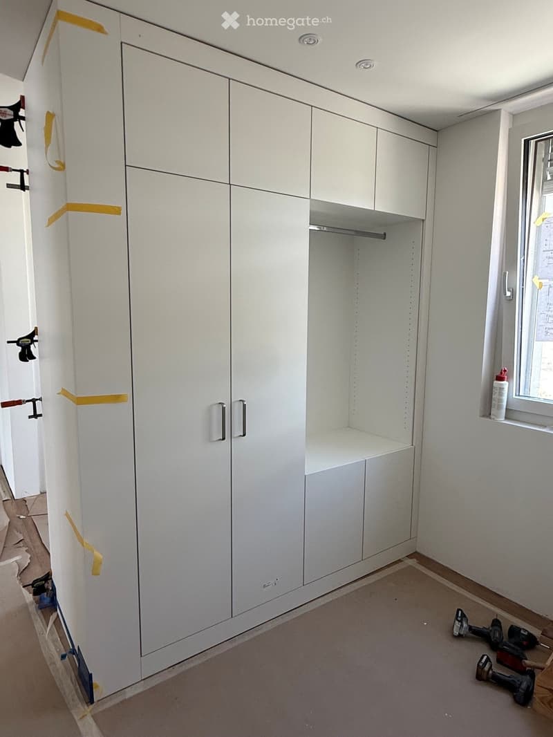 Empty room with white built-in wardrobes, a window, and construction tools on the floor.