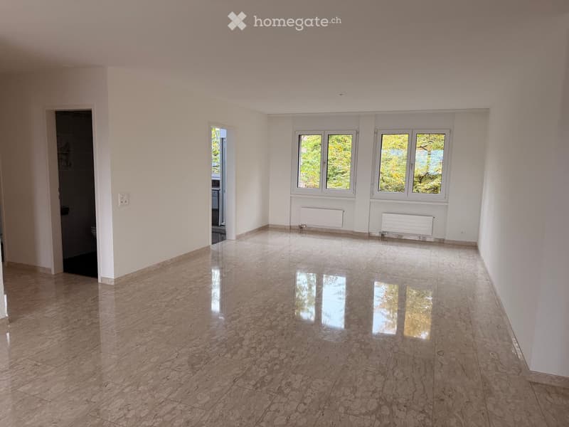 Empty room with polished marble flooring, white walls, large windows with white frames, and a door leading to another room.