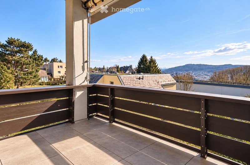 Balcony with wooden railing, tiled floor, and scenic view of city and mountains.