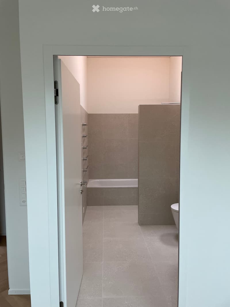 Modern bathroom with a bathtub and toilet, featuring light-colored tiles and a sleek design.