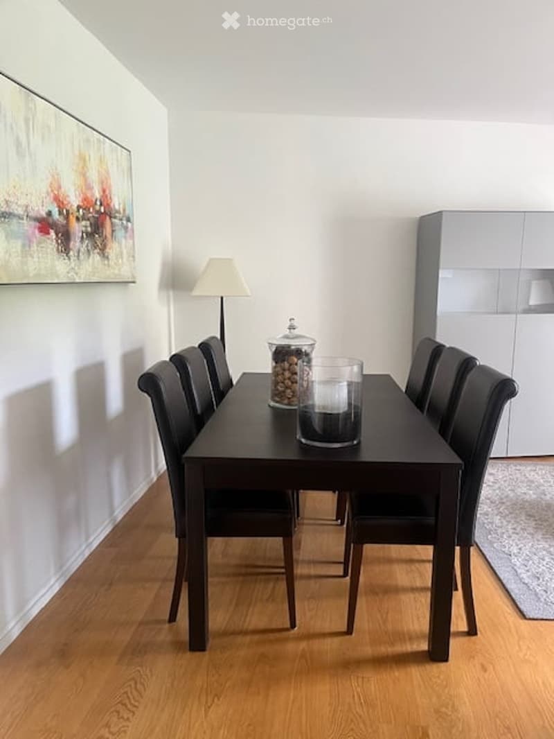 Dining room with a dark wooden dining table surrounded by black chairs, a floor lamp, and a decorative candle holder on the table. A modern white cabinet is visible in the background.