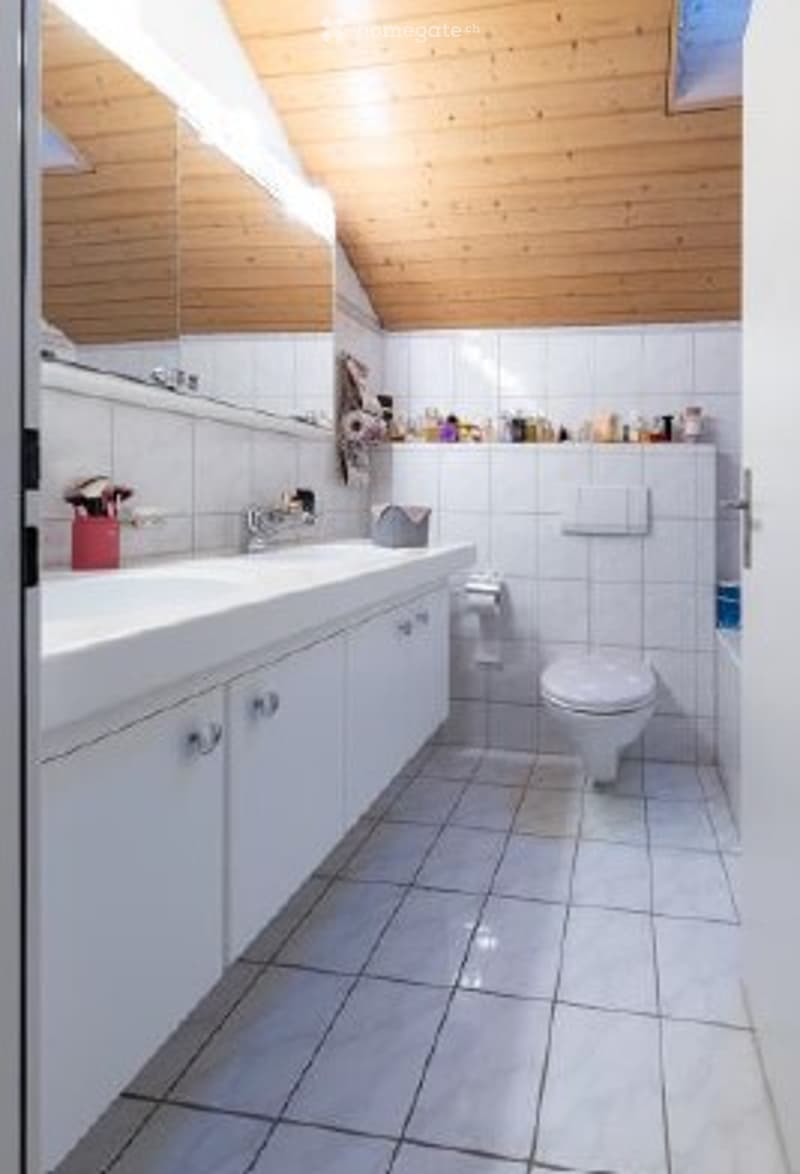 white tiled floor, white tiled walls, wooden ceiling, double sink, mirror, toilet, roll of toilet paper