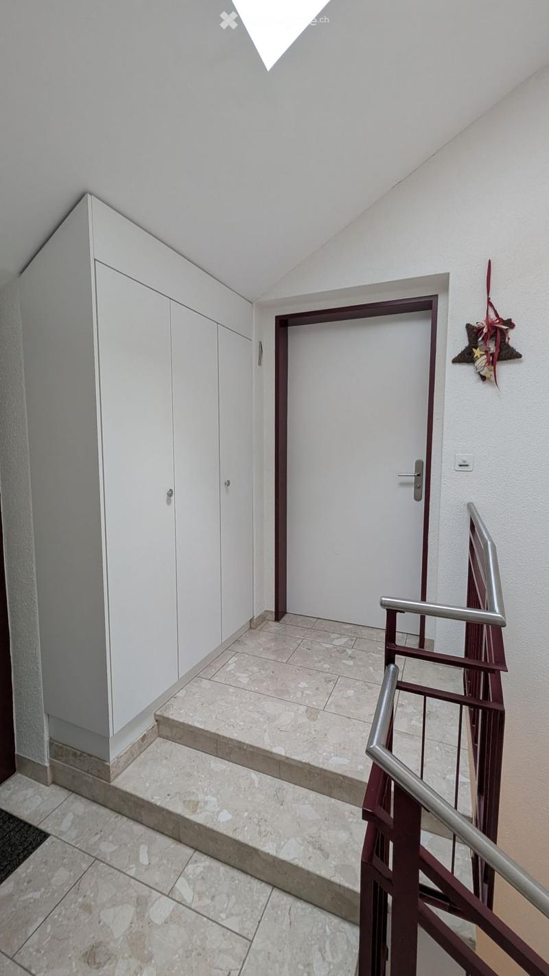 Tiled floor, two sets of white doors, brown railings, modern staircase, white walls.