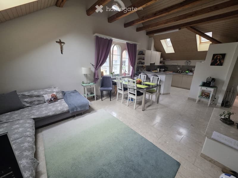 Open-plan living and dining area with exposed wooden beams, a sofa, dining table with chairs, kitchen area, and decorative items.
