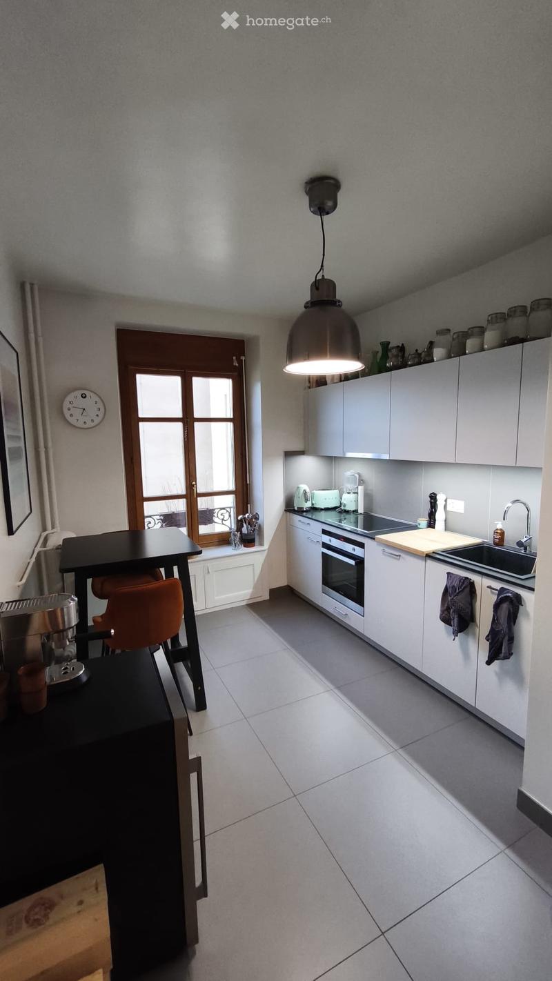 Modern kitchen with white cabinets, stainless steel appliances, a black dining table with orange chairs, and a large window with wooden frame.