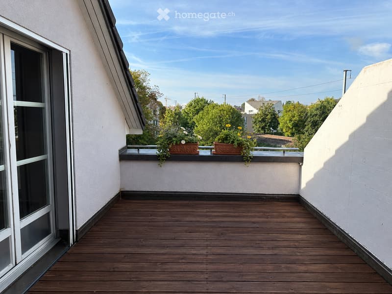 Balcony with wooden decking, white walls, and two flower pots on the railing.