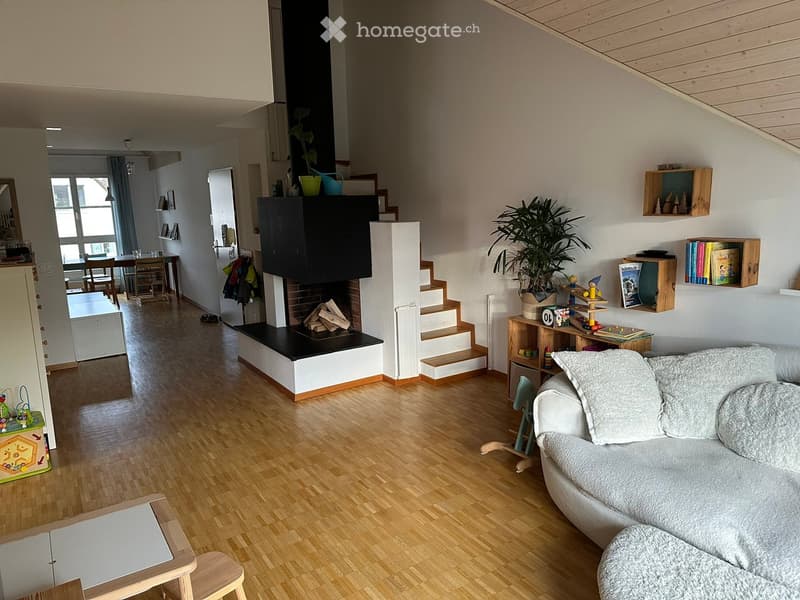 Living room with wooden flooring, a white sofa with an ottoman, a small wooden stool, a dining area with a table and chairs, a fireplace with wood logs, and various decorative items including plants and bookshelves.