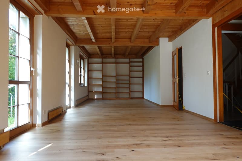 Empty hallway with wooden flooring, white walls, large windows, and built-in wooden shelving unit.