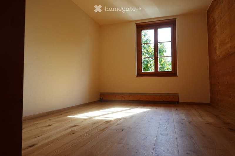 Empty room with wooden flooring, light-colored walls, and a single window with wooden frame letting in natural light.