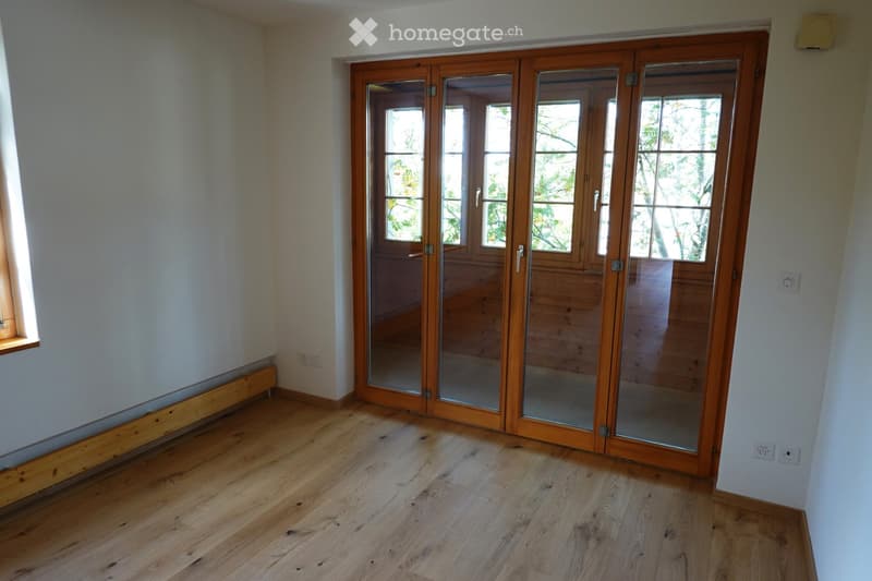 Empty room with wooden flooring, white walls, and large glass sliding doors leading outside.