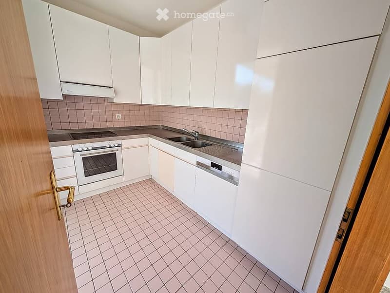 Modern kitchen with white cabinets, tiled backsplash, stainless steel sink, oven, and dishwasher.