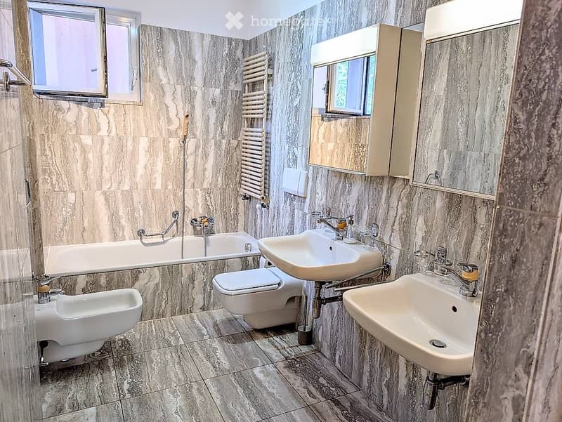Modern bathroom with marble tiles, bathtub, double sink, toilet, bidet, and a radiator.