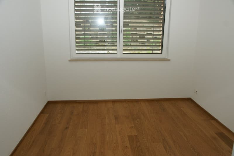 Empty room with wooden flooring and white walls, featuring a single window with blinds.