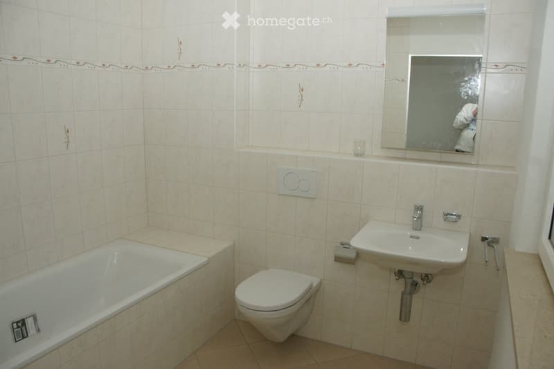 Bathroom with beige tiled walls, a bathtub, toilet, sink, and a mirror above the sink. The walls feature a decorative border with small red accents.