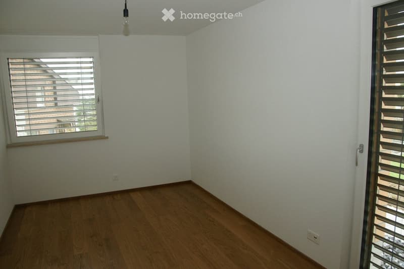 Empty room with light-colored walls, wooden flooring, and two windows with blinds. No furniture or equipment present.