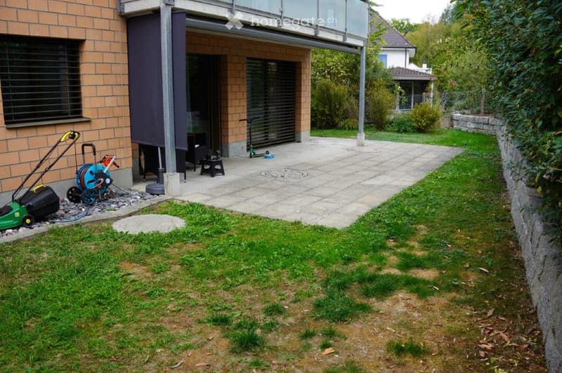 Garden area with a lawn, patio, and various outdoor equipment including a lawnmower, hoses, and a scooter.