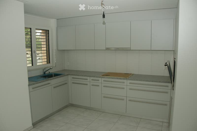 Modern kitchen with white cabinets, granite countertops, and tiled flooring. Features a sink with a modern faucet and a cutting board on the counter.